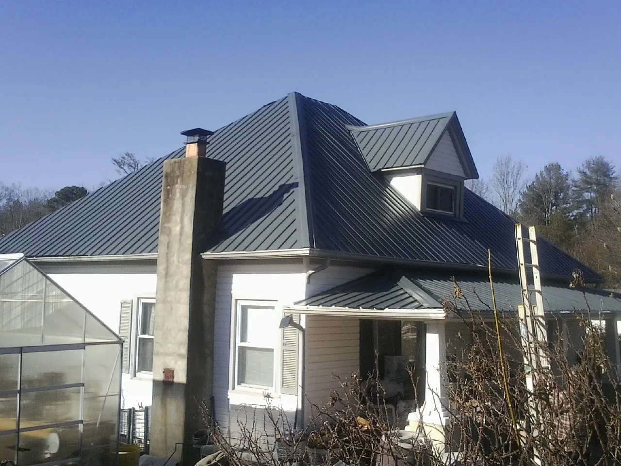 Dark blue standing seam metal roof on a white farmhouse with dormer — Slate & Tile Roof Repair by Roofing Brothers in Barnard