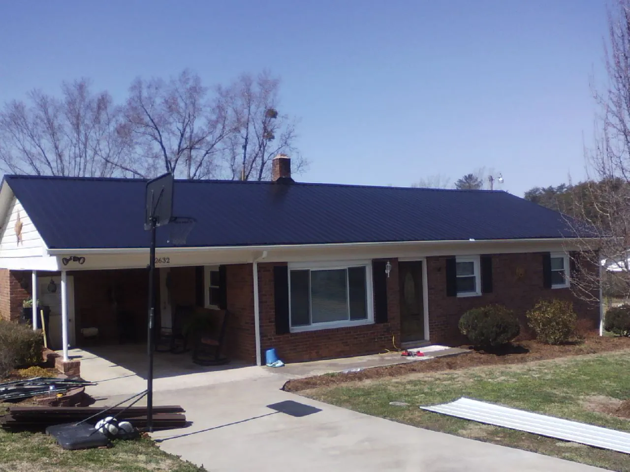 Finished dark blue metal roof on a brick ranch with a carport in Barnard
