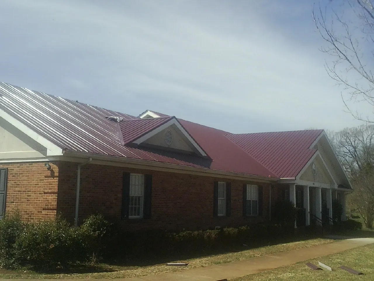 Red metal roof with gabled entries on a long brick building, from a Hail Damage Roof Repair job in Barnard