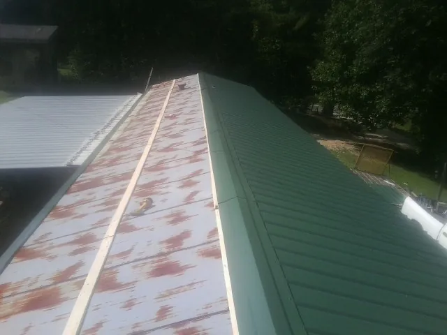 Old rusted panels beside newly installed green metal roofing — Wind Damage Roof Repair by Roofing Brothers in Barnard