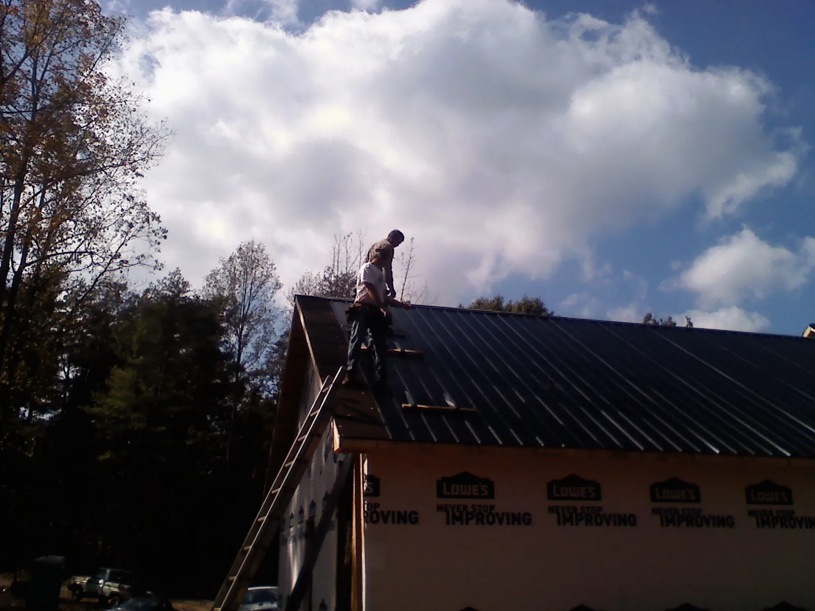 Roofer fastening dark metal panels high against a cloudy sky, from a Roof Inspection job in Barnard