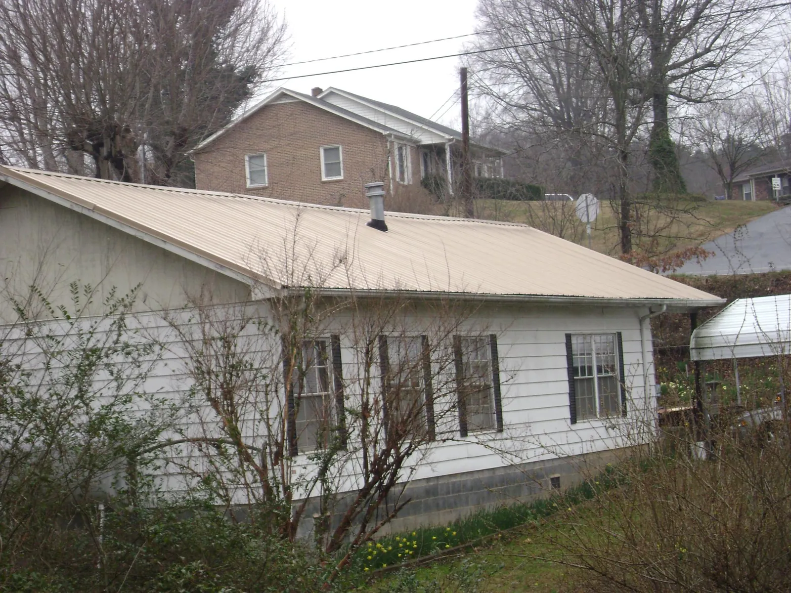 Tan metal roof on a white sided house set into a hillside — Commercial Roofing by Roofing Brothers in Barnard