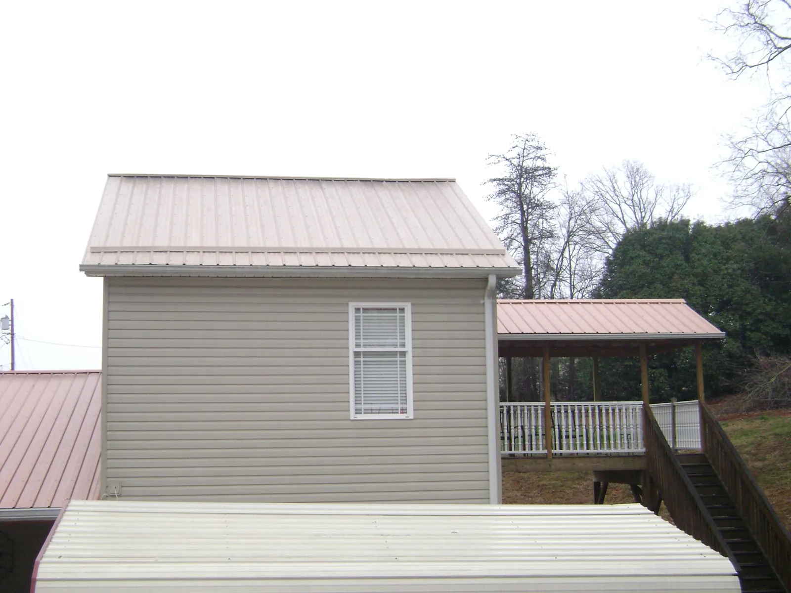 Tan metal roofs on a two story addition and attached porch, from a Roof Replacement job in Barnard